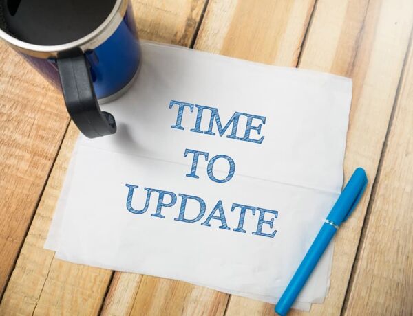 Ein Zettel auf dem "Time To Update" steht liegt mit Stift und Tasse auf einem Holz-Tisch
